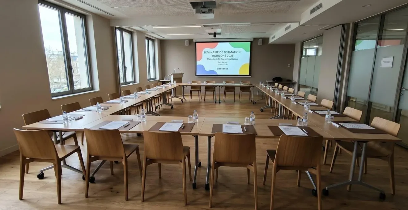 Salle de séminaire moderne aménagée en configuration U avec chaises vides disposées en fer à cheval face à un écran de présentation