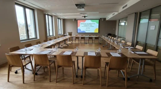 Salle de séminaire moderne aménagée en configuration U avec chaises vides disposées en fer à cheval face à un écran de présentation